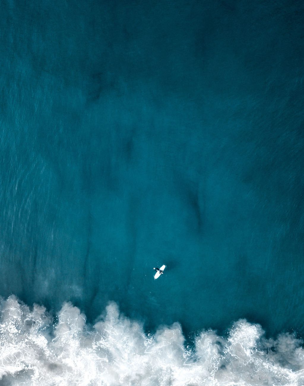 An aerial overhead vertical shot of beautiful ocean waves with a plane flying above